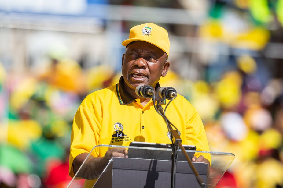 Black man in a yellow shirt and hat speaking at a podium