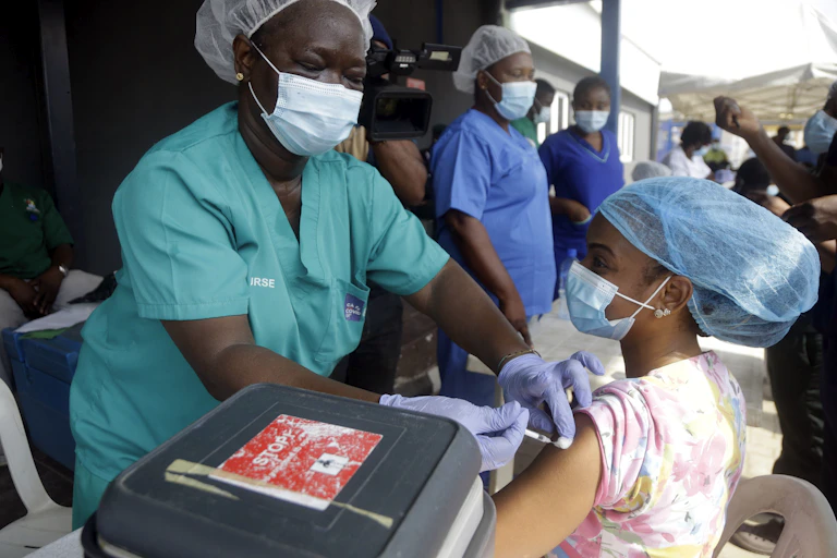 Hospital staff in scrubs and hair nets given vaccine doses to people.