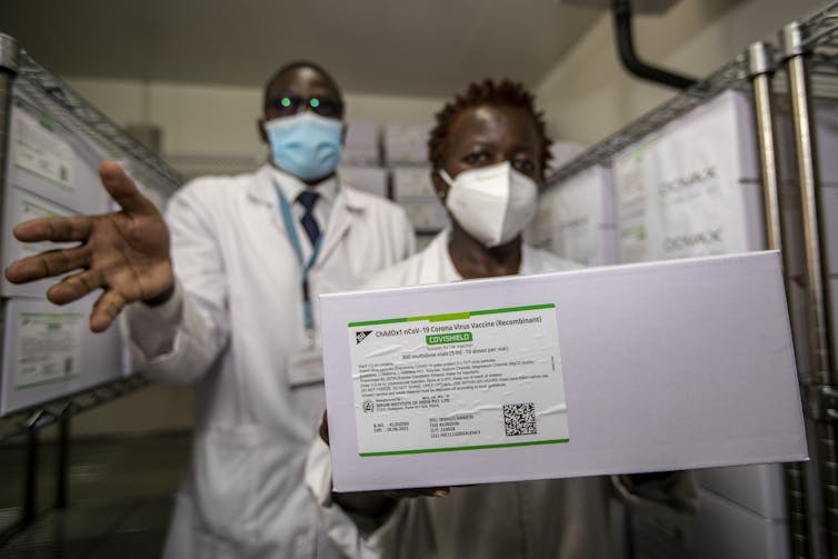 Two people in lab coats hold a box showing the label