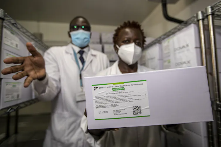 Two people in lab coats hold a box showing the label