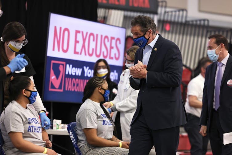 New York Gov. Andrew Cuomo walks past students getting vaccinated at Suffolk County Community College