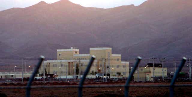 Large building behind security fence with mountains in background