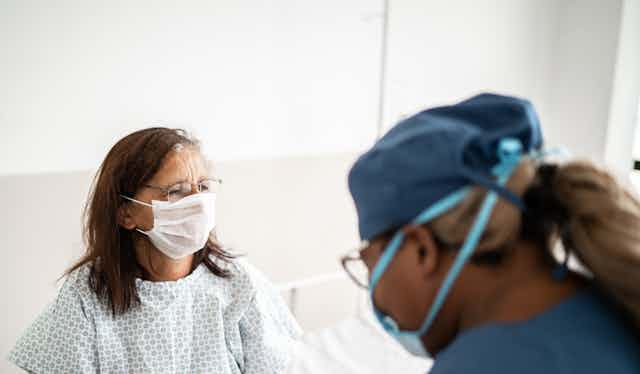 A hospital patient wearing a mask talks to her doctor.