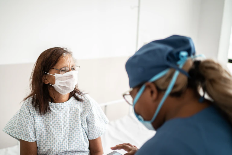 A hospital patient wearing a mask talks to her doctor.