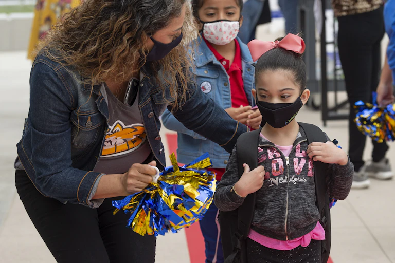 Students wearing masks get escorted to school by a teacher.