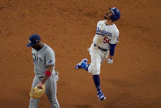 Los Angeles Dodgers player Mookie Betts shows jubilation after hitting a home run in the 2020 World Series while a member of the Tampa Bay Rays looks dejected while 