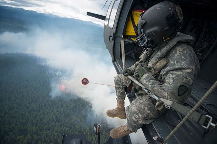 View of a burning forest from a helicopter with a soldier sitting in the open helicopter door