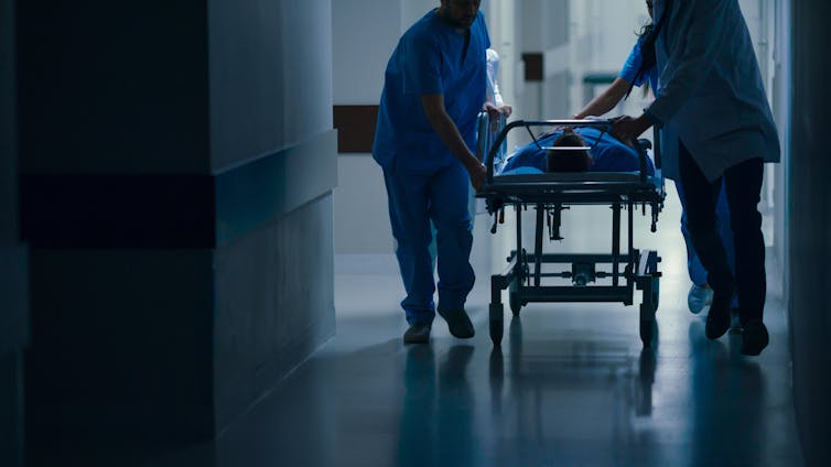 Two health-care workers move a patient through a hospital corridor.