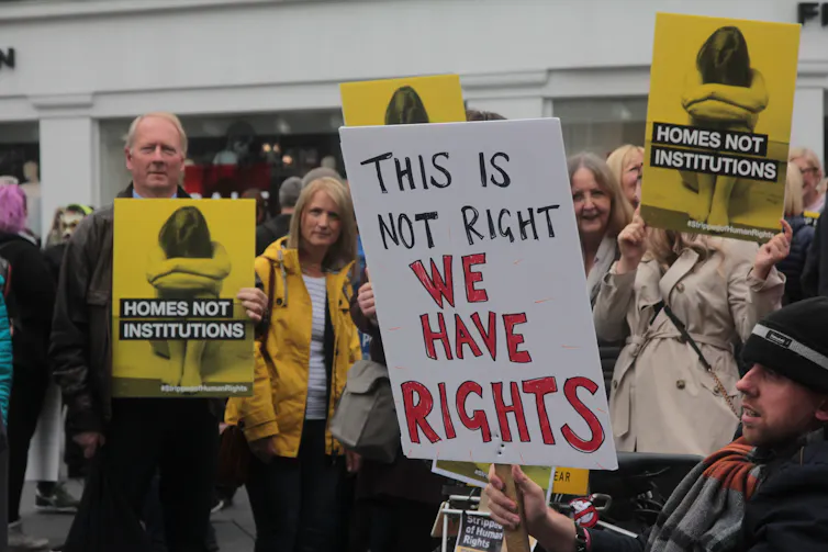 Disability rights protesters in Newcastle holding signs that say 'ths is not right we have rights' and 'homes not institutions'