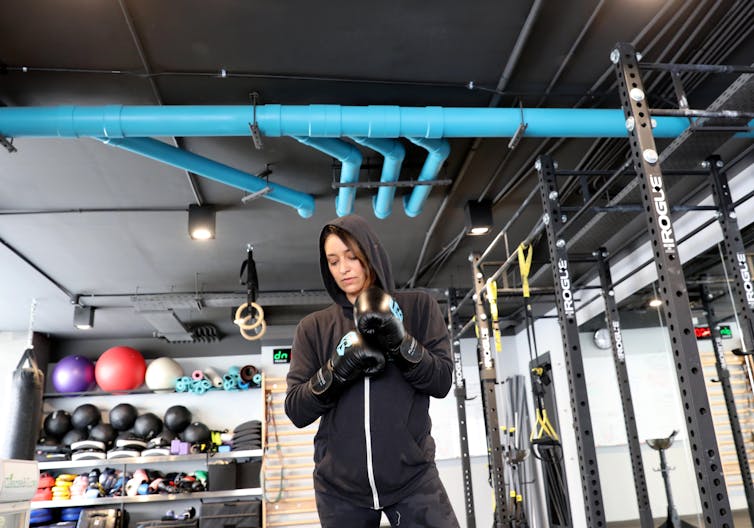 A woman in a gym wearing boxing gloves and a hoody.