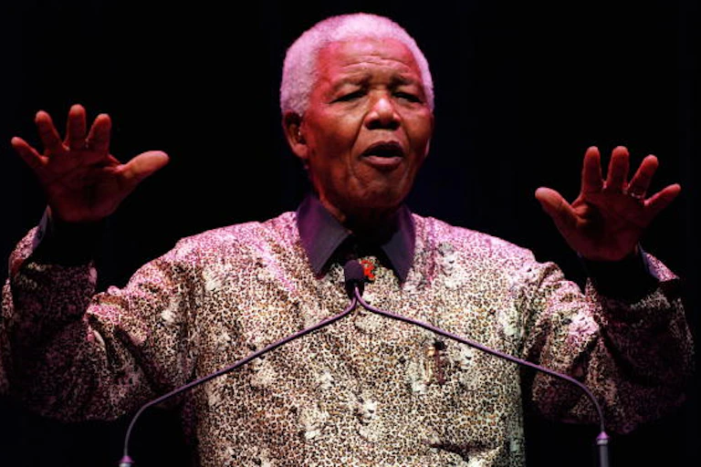 An old, grey-haired gestures with his raised arms atwhille speaking on a podium
