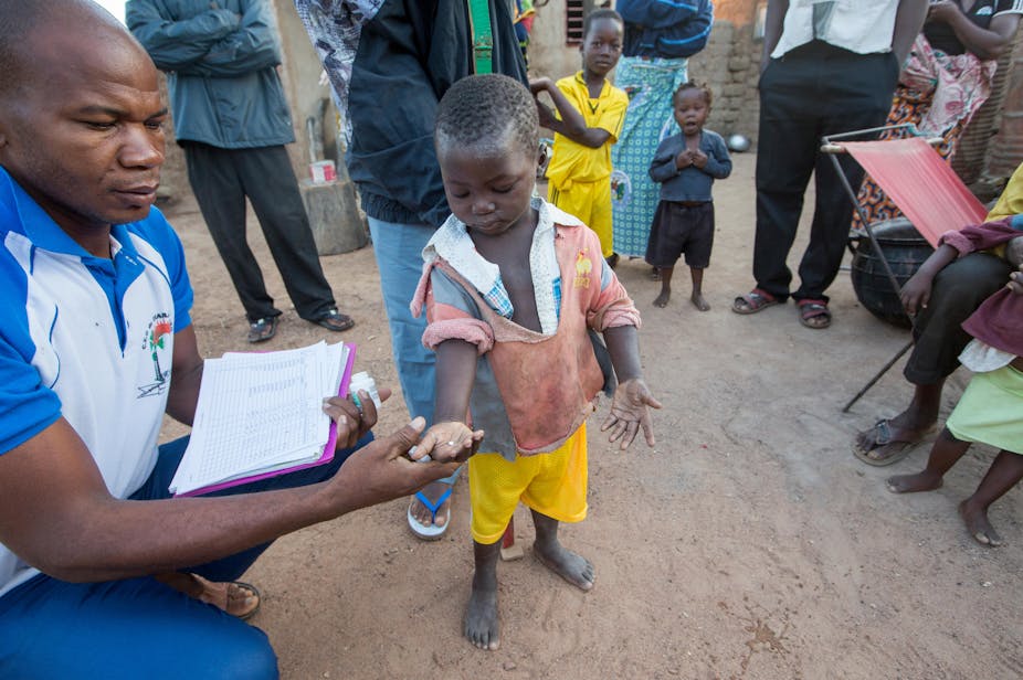 In Burkina Faso, a small boy is given a pill by a health worker as family look on.