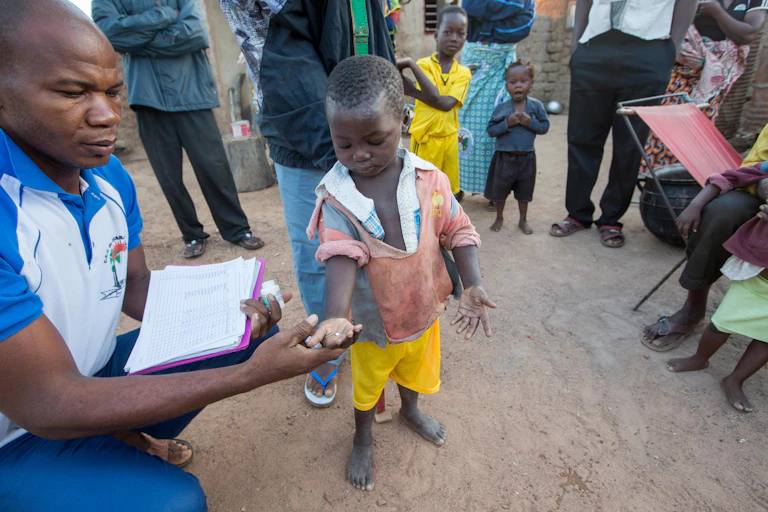 In Burkina Faso, a small boy is given a pill by a health worker as family look on.