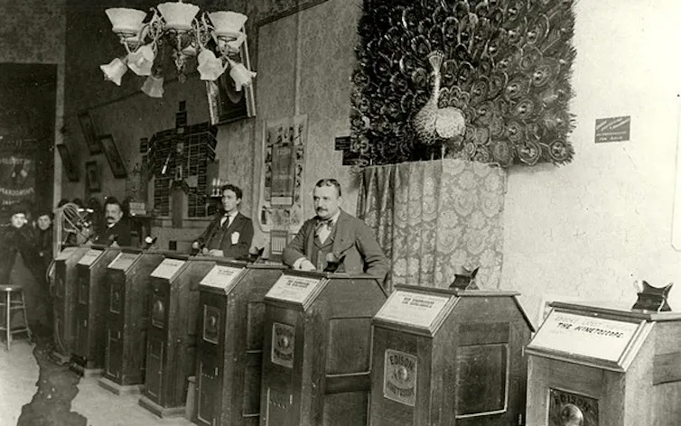 Men standing at Kinetoscopes.