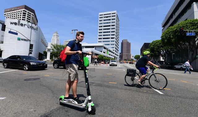 A car, e-scooter rider and cyclist share the road in Los Angeles