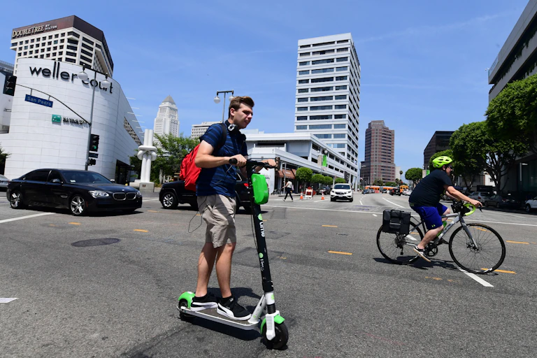 A car, e-scooter rider and cyclist share the road in Los Angeles