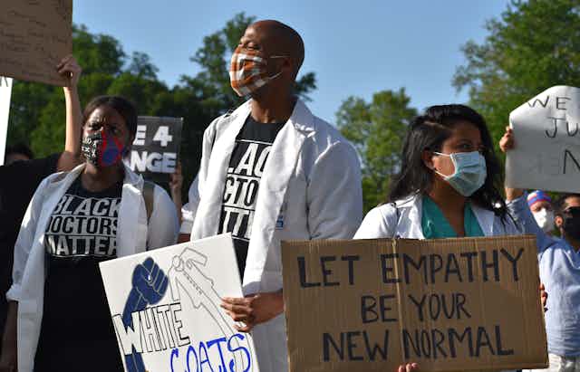 Health care workers wearing white coats protest racist health care.