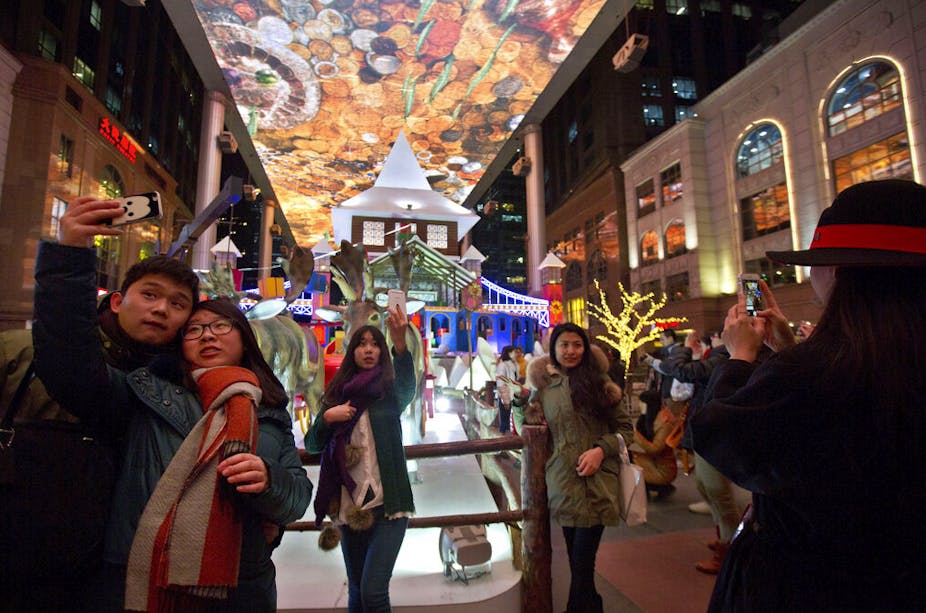 Shoppers pose for selfies near Christmas-themed decorations in a colorfully decoracted shopping mall in Beijing, China.