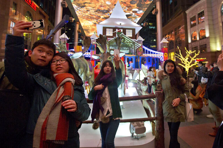 Shoppers pose for selfies near Christmas-themed decorations in a colorfully decoracted shopping mall in Beijing, China.