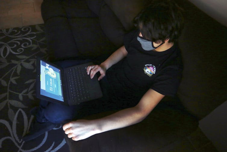 A young student wearing a mask uses a laptop