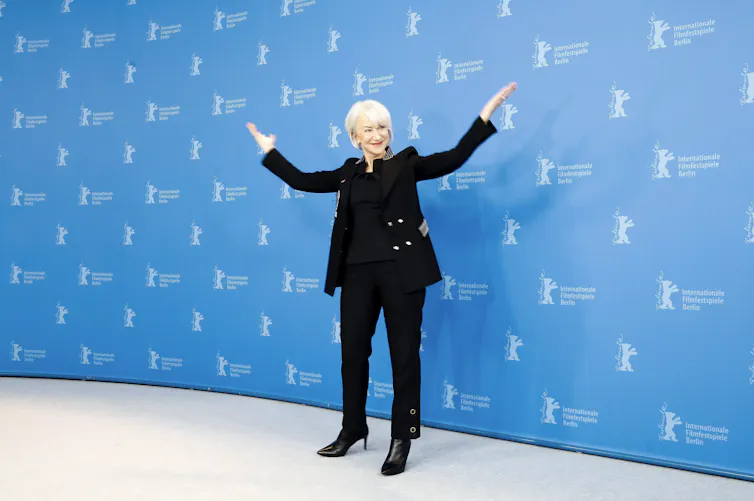 Helen Mirren in a dark suit with gold buttons and stiletto heel boots