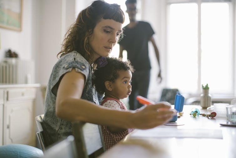 A woman holds a child in her lap while doing paperwork