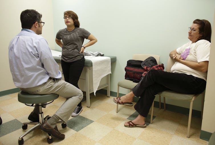 A teenage transgender boy with his mother speaking with a doctor.