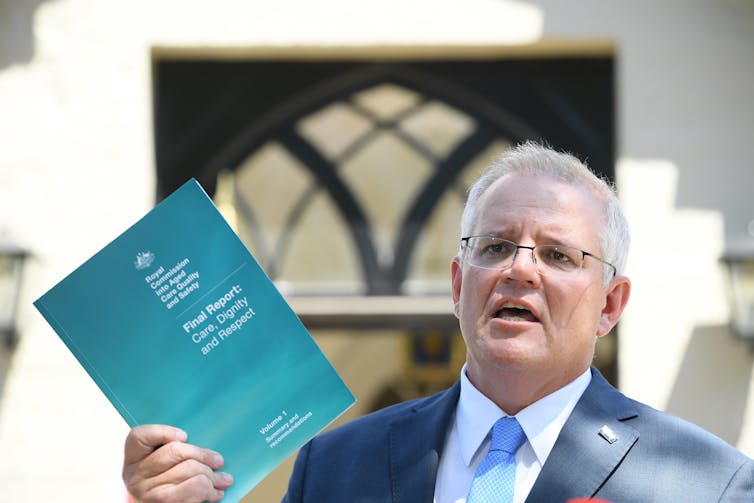 Prime Minister Scott Morrison holds up a copy of the aged care royal commission's final report.