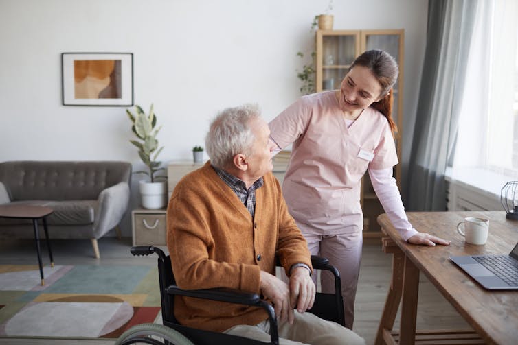 A carer speaks to an elderly man in a wheelchair at a retirement home.