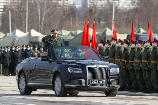 A Russian general in a convertible limousine salutes Russian troops as he drives past.