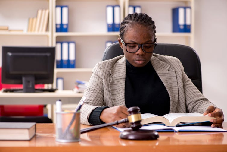 Black woman solicitor reads a law book at her desk.
