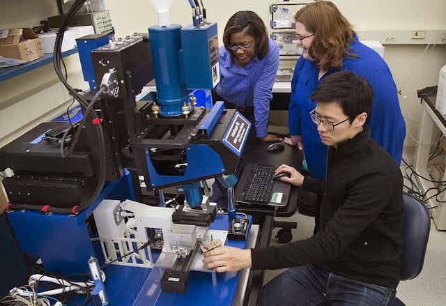 Researchers working in a lab studying effect of heat on hair with infrared microscope.
