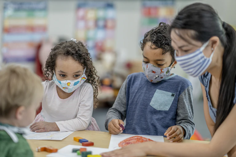 A teacher colors and plays with little kids.
