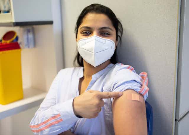 masked woman points to her vaccine bandaid