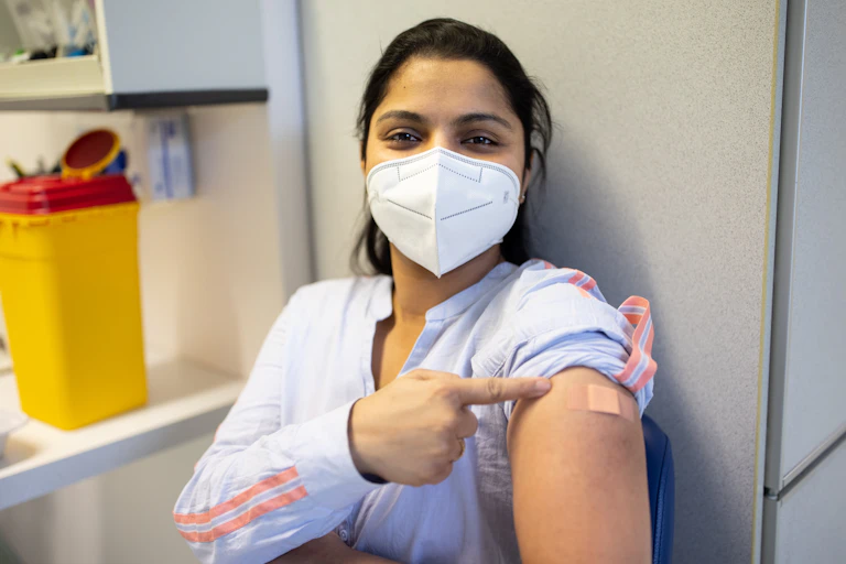 masked woman points to her vaccine bandaid