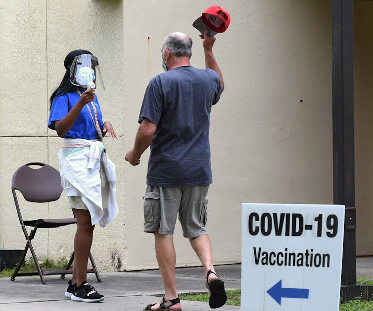 man removes hat for temperature check at COVID-19 vaccination site