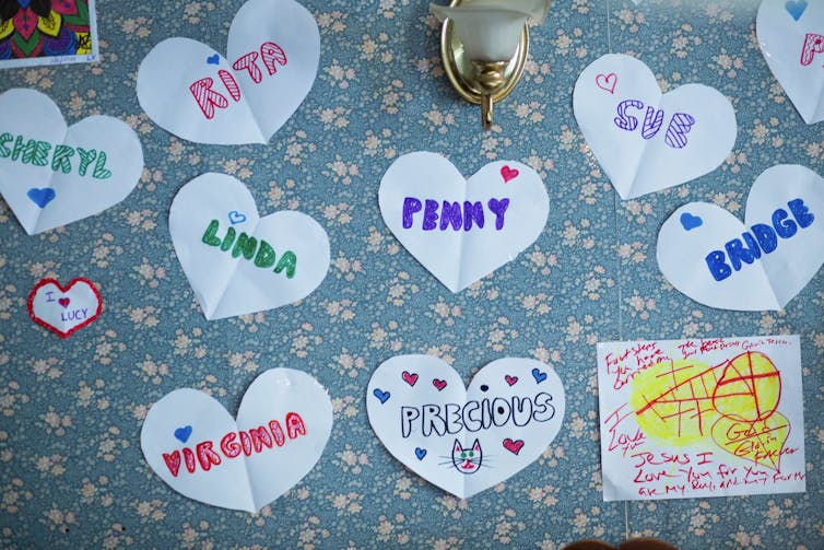 Paper hearts with women's names on them on a flowery bulletin board.