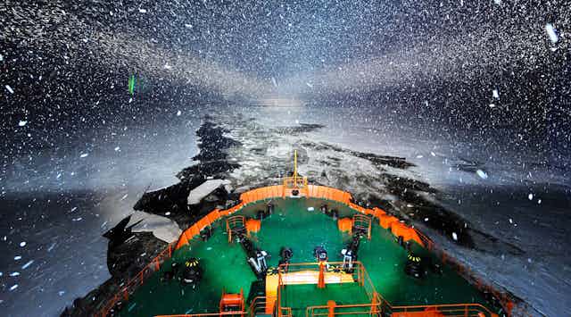 An icebreaker at night with the open channel of water through the ice behind it