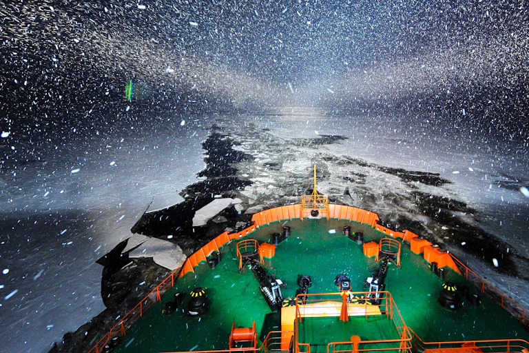 An icebreaker at night with the open channel of water through the ice behind it