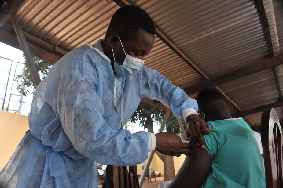 A man getting an injection in his upper arm from a medical practitioner wearing a face mask.