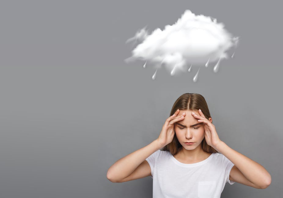 Woman clutching her head in pain while storm clouds form above her head.