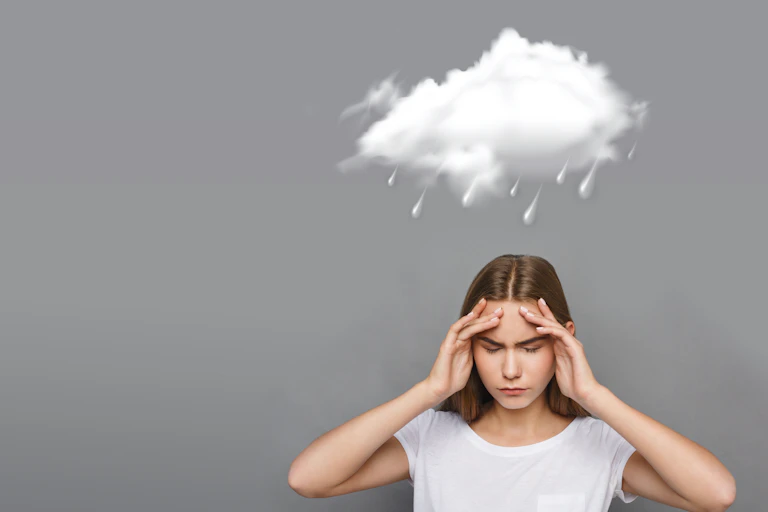 Woman clutching her head in pain while storm clouds form above her head.