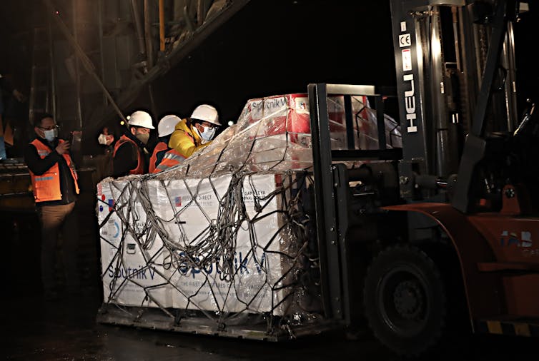 Workers in hard helmets unload a shipment of Sputnik V vaccines.