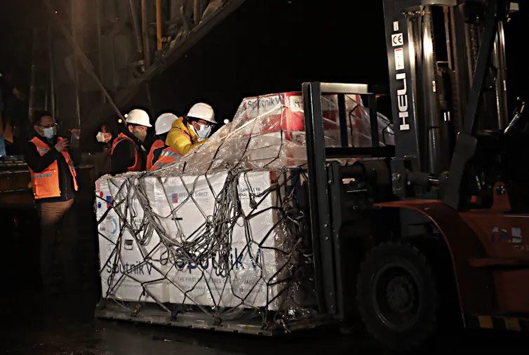 Workers in hard helmets unload a shipment of Sputnik V vaccines.
