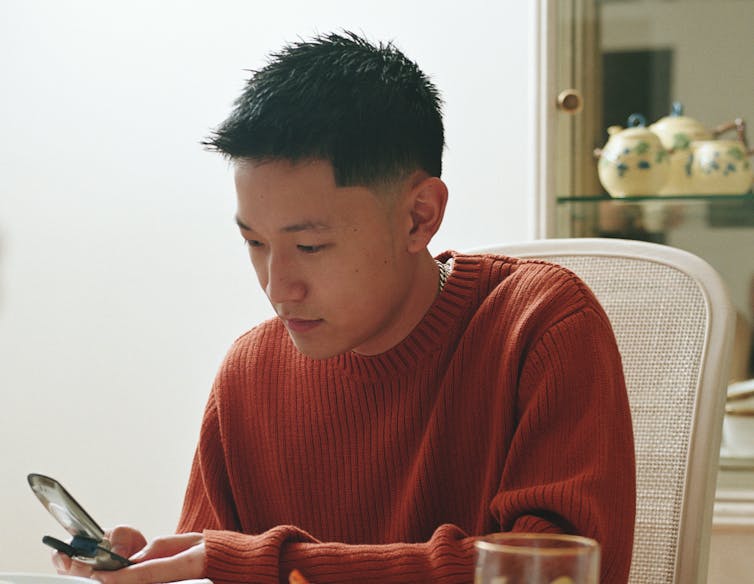 An Asian American teen looks at his cell phone.