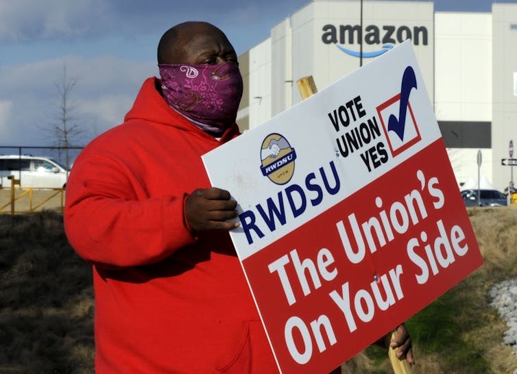 A man in a red coat holding a pro-union sign stands outside an Amazon facility in Bessemer, Alabama