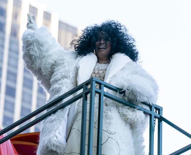 Diana Ross, wearing white fur, gloves and a silve and white dress.