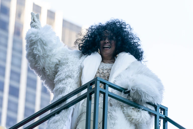 Diana Ross, wearing white fur, gloves and a silve and white dress.