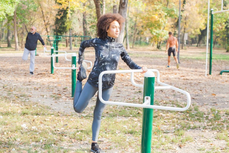 A woman stretches on outdoor exercise equipment.