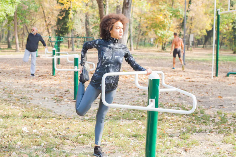 A woman stretches on outdoor exercise equipment.